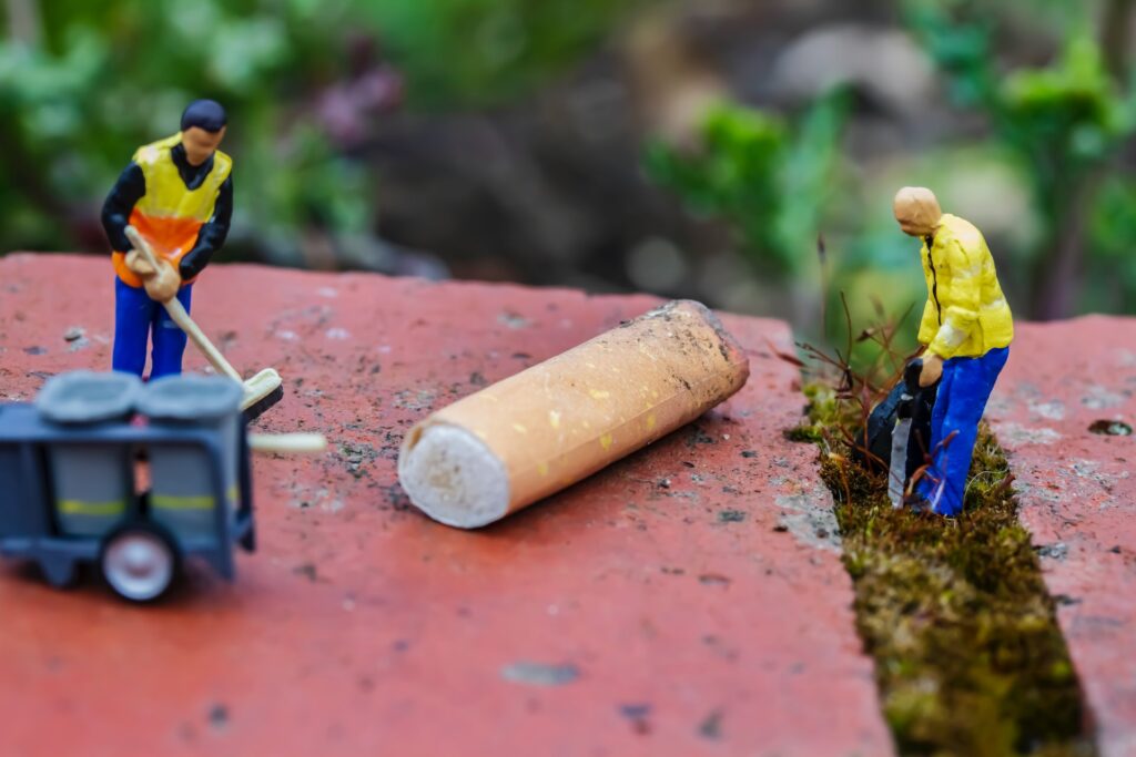 Two tiny figures clearing up a huge cigarette butt